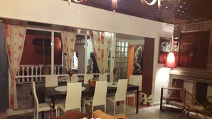 A dining area with a table set for four, surrounded by white chairs. There is a wooden bench with a decorative plant in the foreground.