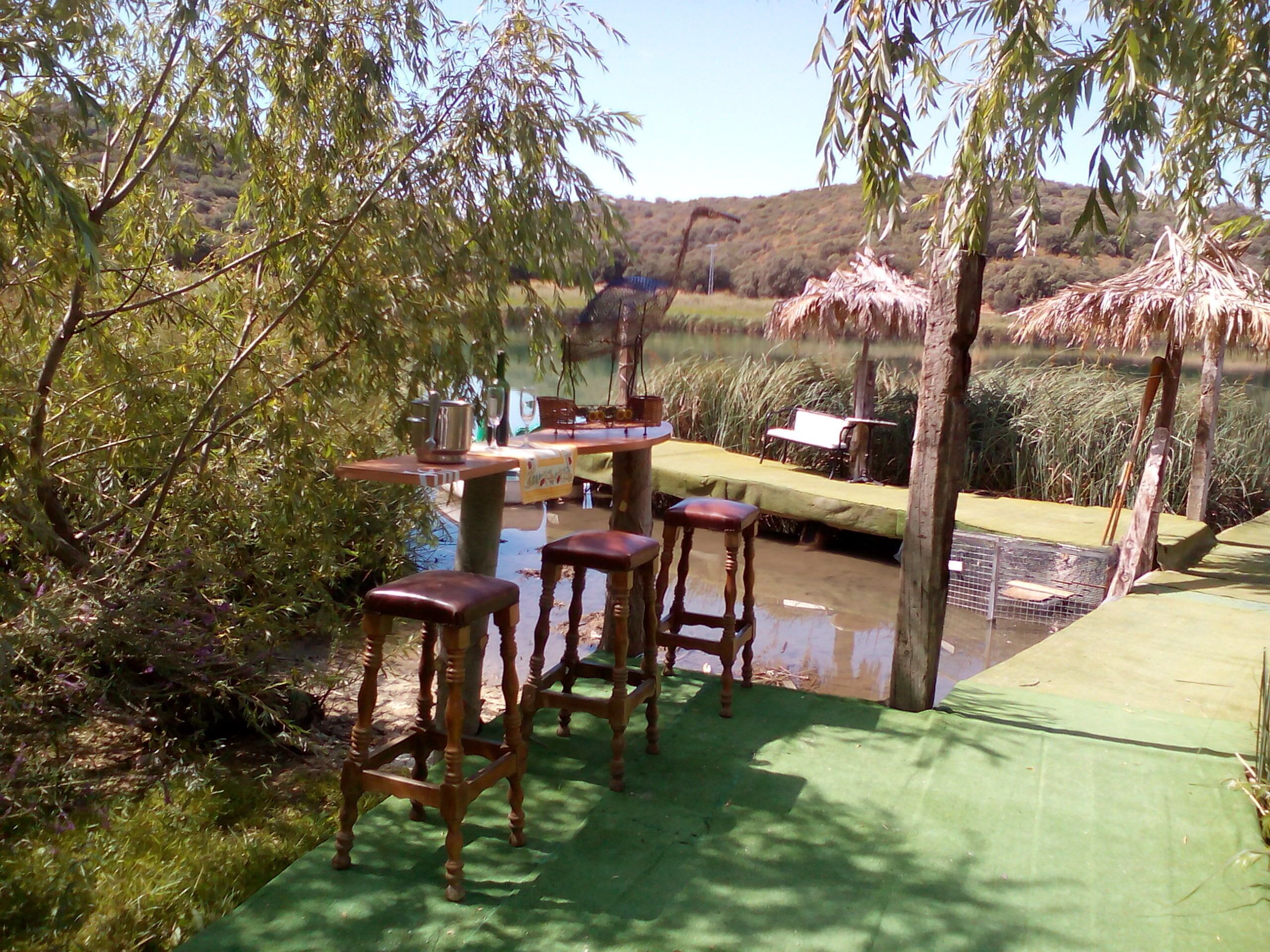 An outdoor dining area with a table and chairs, surrounded by greenery and a water feature.