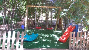 A wooden swing set with a green artificial turf surface, surrounded by a wooden fence.