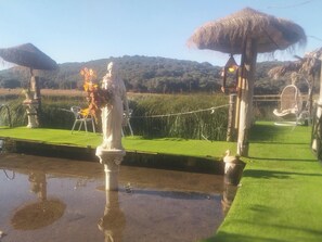 A statue on a platform with a grassy area and a water feature. - House at the edge of the lagoon with a dock........................ (Ruidera)