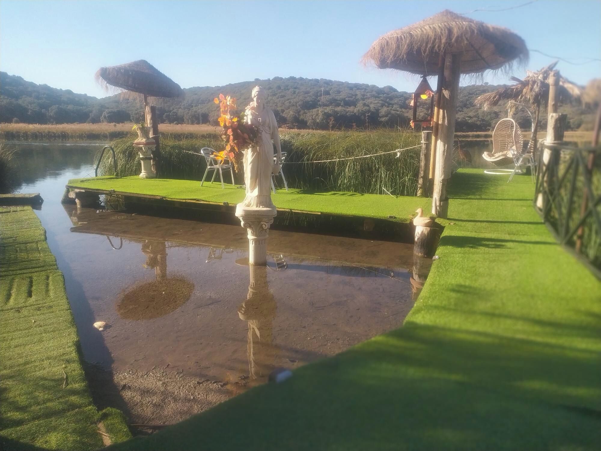 Un espacio al aire libre tranquilo con un estanque, una estatua y una construcción con techo de paja.