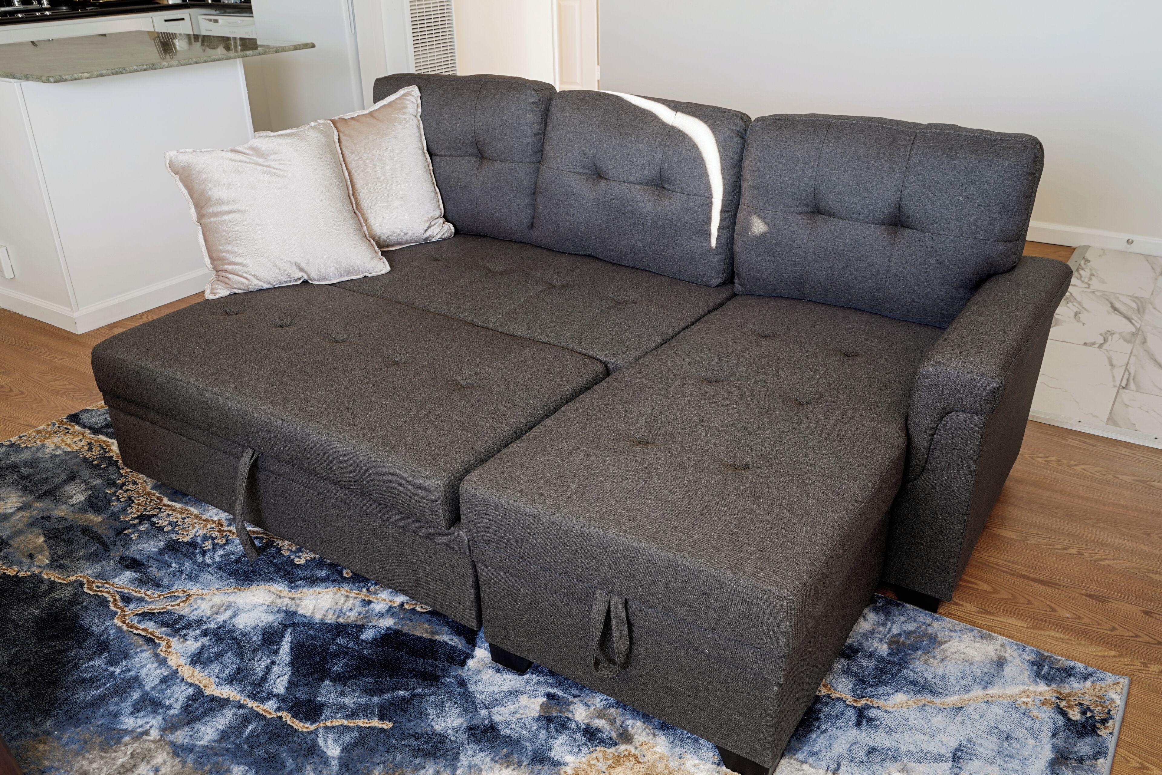 A sectional sofa with a chaise, a patterned rug, and a kitchen area in the background.