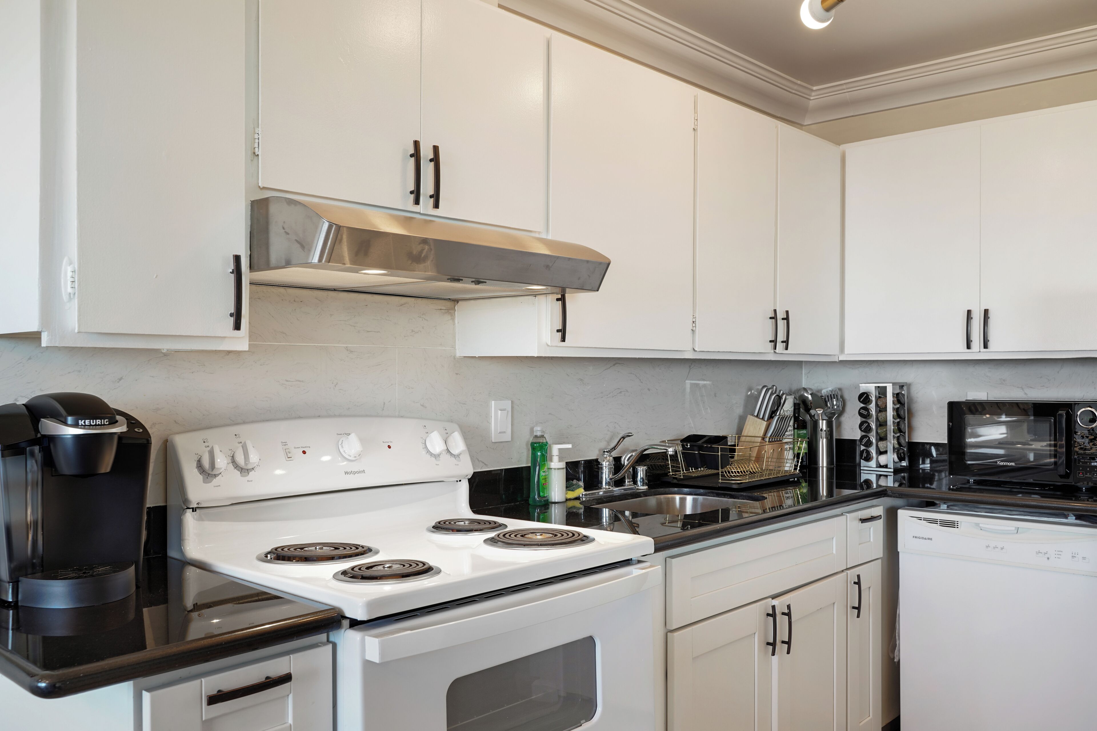 A kitchen with white cabinets, a white stove, a coffee maker, and a dishwasher.