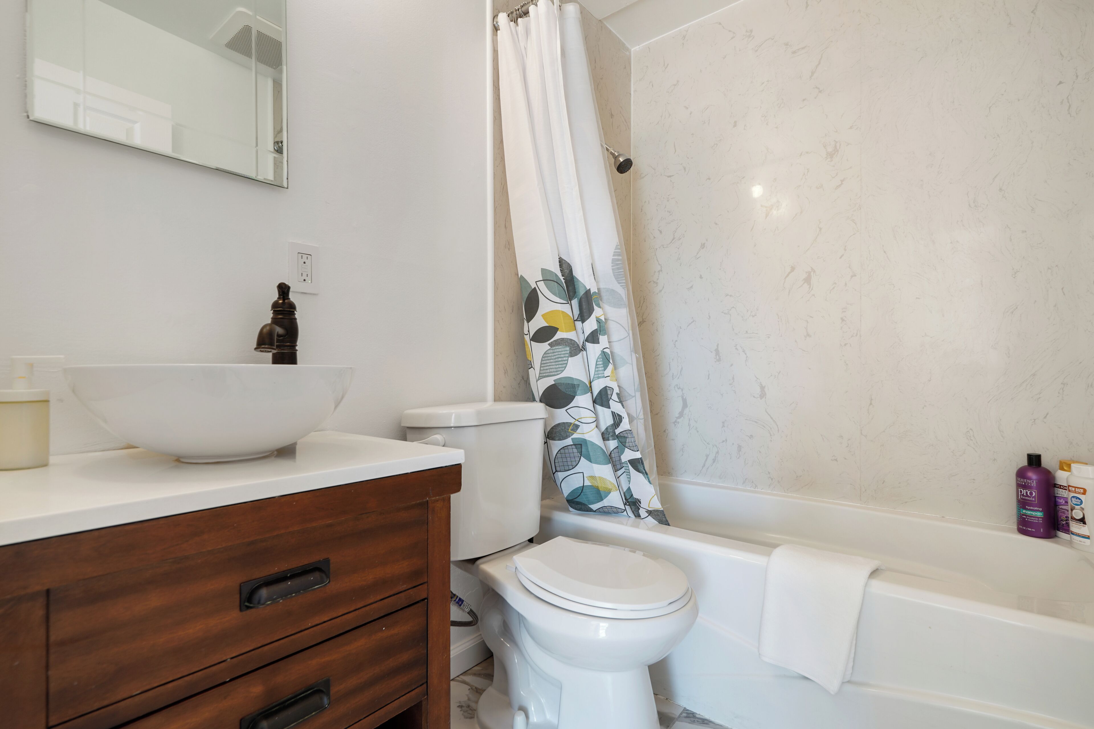 Een badkamer met een witte wasbak, een houten wastafelmeubel, een toilet en een bad.