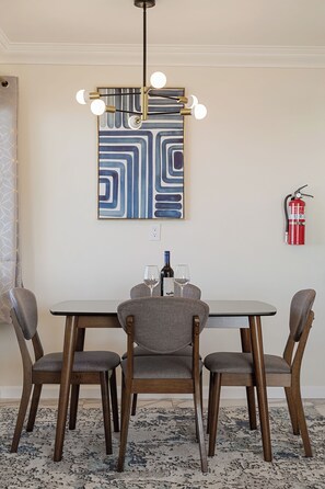 Un coin repas comprenant une table, quatre chaises, un lustre moderne, un extincteur et un grand tableau abstrait accroché au mur.