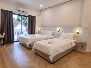 A hotel room with two beds, a desk, and a view of a building outside. - Lunar Hostel (Vientiane)