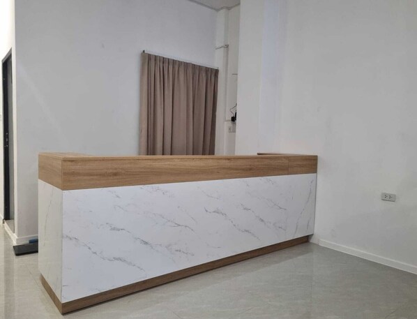 Ein Empfangsschalter mit Marmorplatte und Holzfuß, ein beiger Vorhang und eine weiße Wand.
