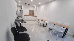 Una sala de conferencias con paredes blancas, un mostrador de recepción y una combinación de sillas negras y blancas alrededor de mesas rectangulares.