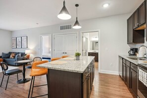 Een moderne keuken met een centraal eiland, donkerhouten kasten en een eethoek met oranje stoelen.