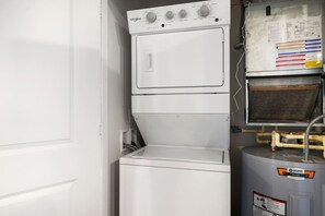 Un lavadero pequeño y blanco con lavadora y secadora Whirlpool, un calentador de agua y un panel de control con instrucciones de seguridad.