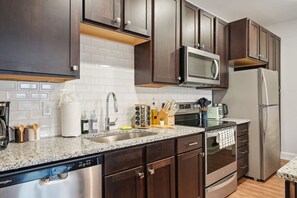 Een moderne keuken met donkerhouten kastjes, een roestvrijstalen koelkast, een magnetron en een vaatwasser.
