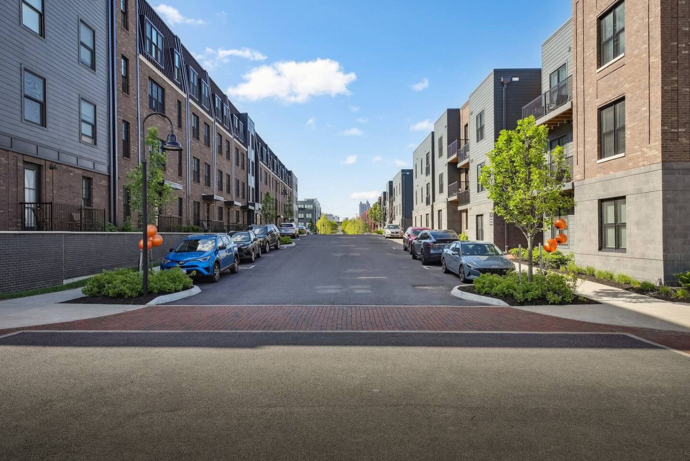 Vista de una calle en una zona residencial con edificios de apartamentos modernos, cielo despejado y coches estacionados.