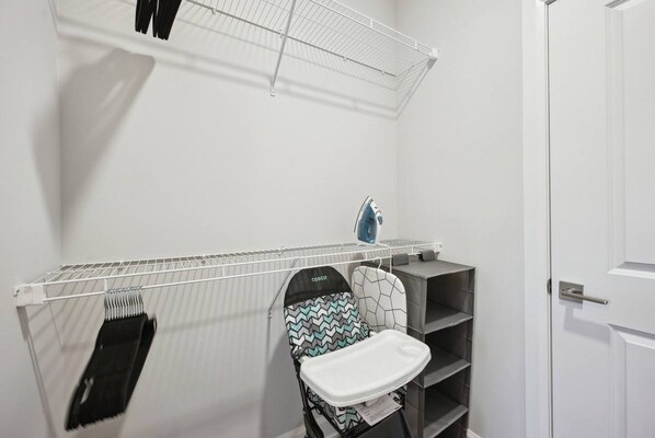 A compact laundry room with a drying rack, ironing station, and a small seating area.