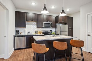Une cuisine moderne avec des meubles de couleur sombre, des appareils en acier inoxydable et un îlot central doté de tabourets de bar.
