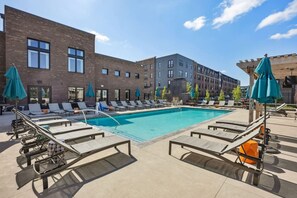 A poolside area with lounge chairs and umbrellas, a brick building, and a clear sky.