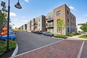 Una calle urbana moderna con edificios de varios pisos, automóviles estacionados y un camino de ladrillos.
