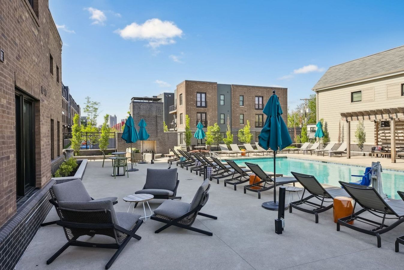 Un espace piscine aménagé sur le toit, avec des chaises longues et des parasols, entouré d’immeubles.