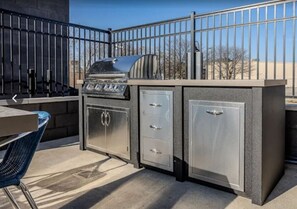 An outdoor kitchen with a grill, storage cabinets, and a dining area with a chair.