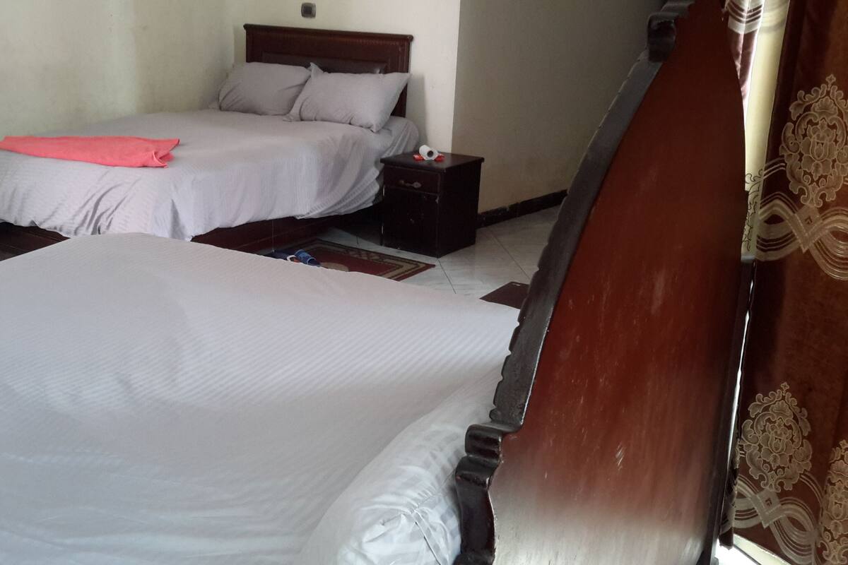 A hotel room with two beds, a nightstand, and a wooden headboard.