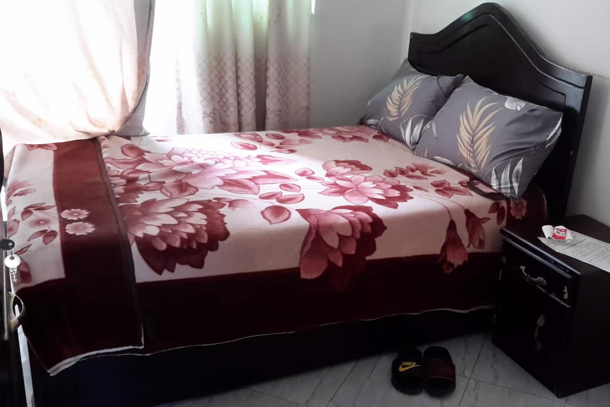 A neatly made bed with a floral bedspread, a dark headboard, and a nightstand with a lamp and a menu.