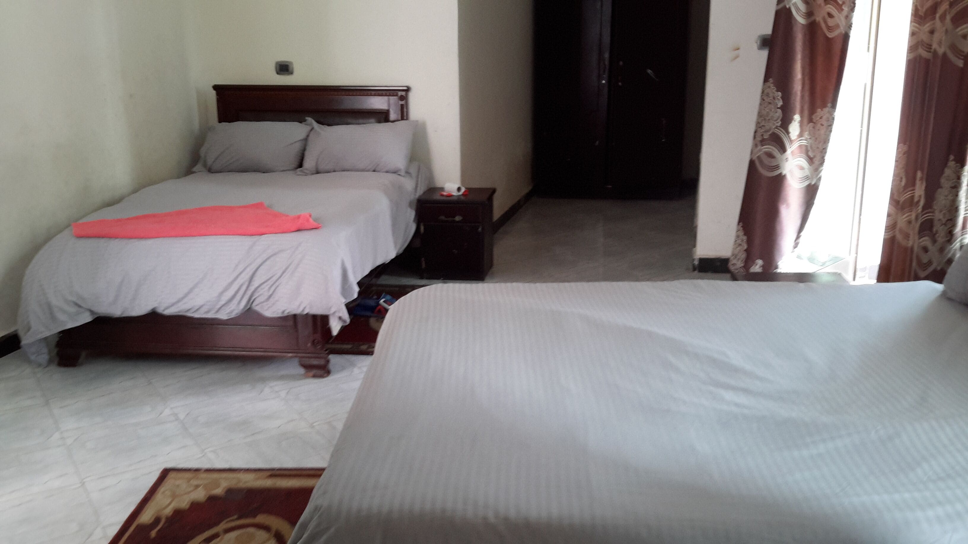 A bedroom with two beds, a nightstand, and a door leading to another room.