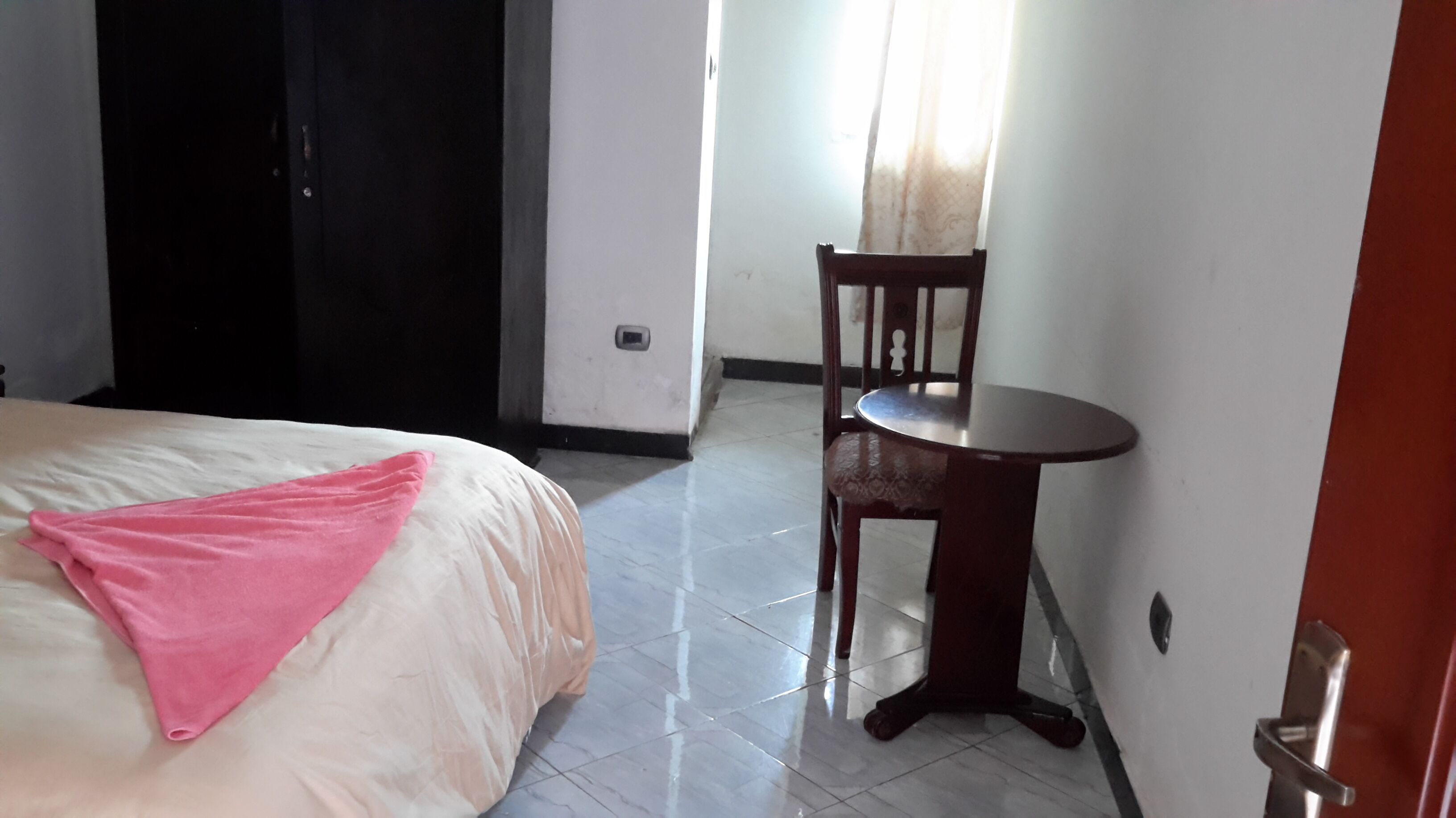 A hotel room with a bed, a small round table, and a chair.