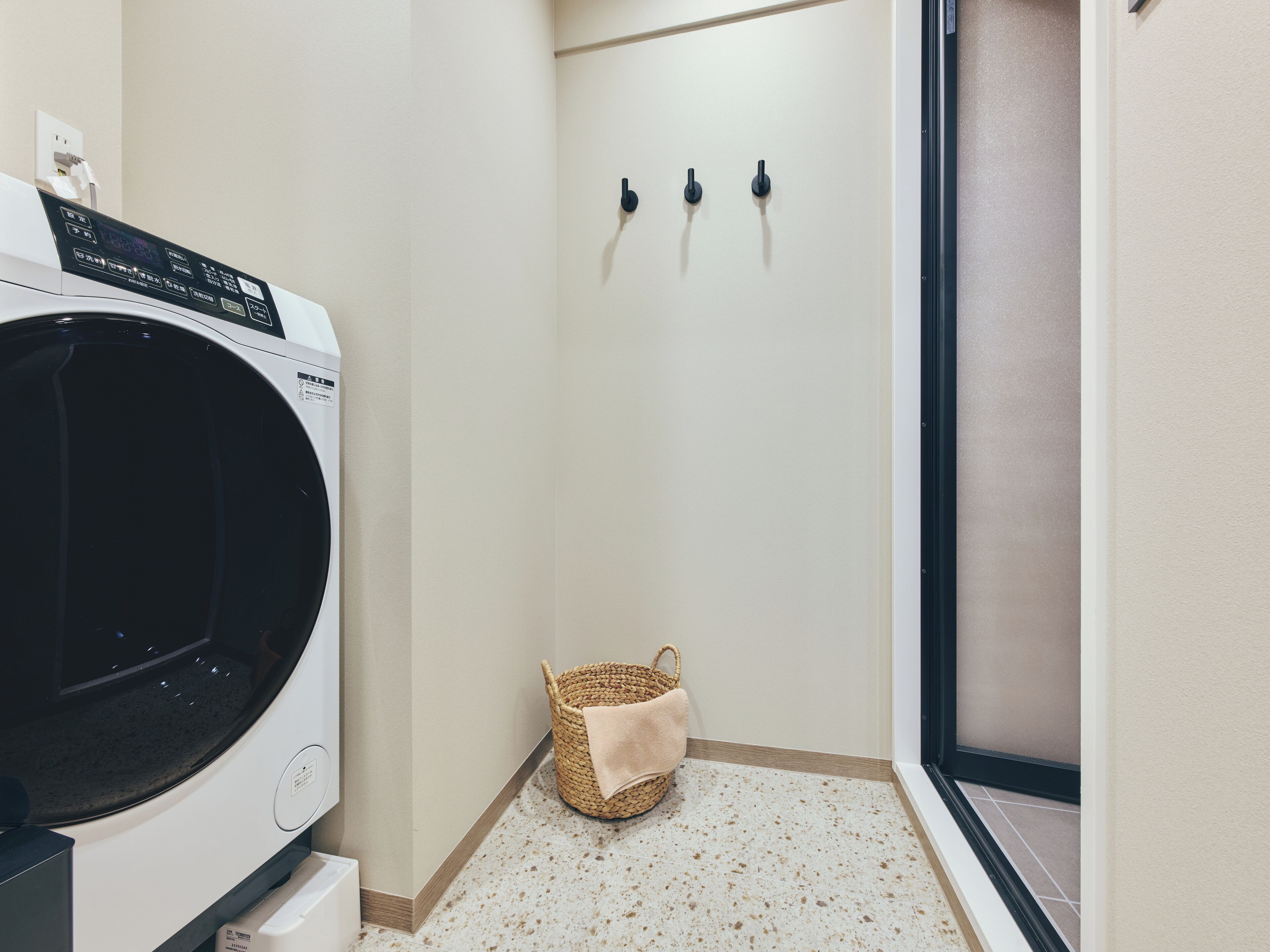 Une buanderie équipée d’un lave-linge, d’un petit panier en osier et d’un porte-serviettes.