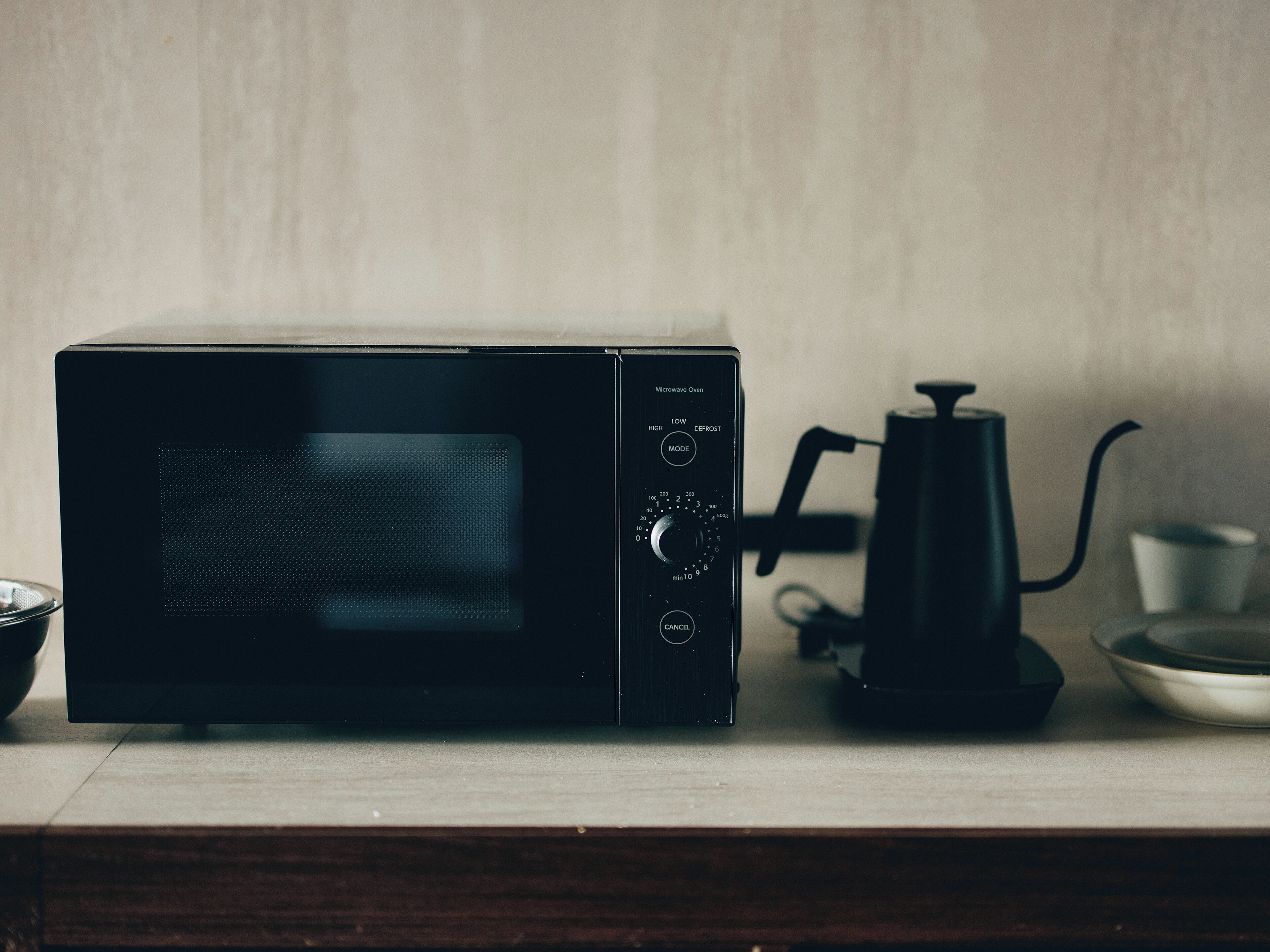 A black microwave oven on a wooden surface with a coffee maker and a bowl nearby.