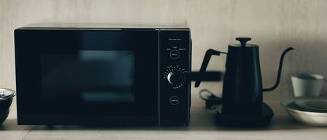 A black microwave oven on a wooden surface with a coffee maker and a bowl nearby.