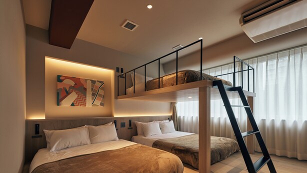 Habitación de hotel moderna con cama estilo loft, una escalera y un amplio ventanal con cortinas.