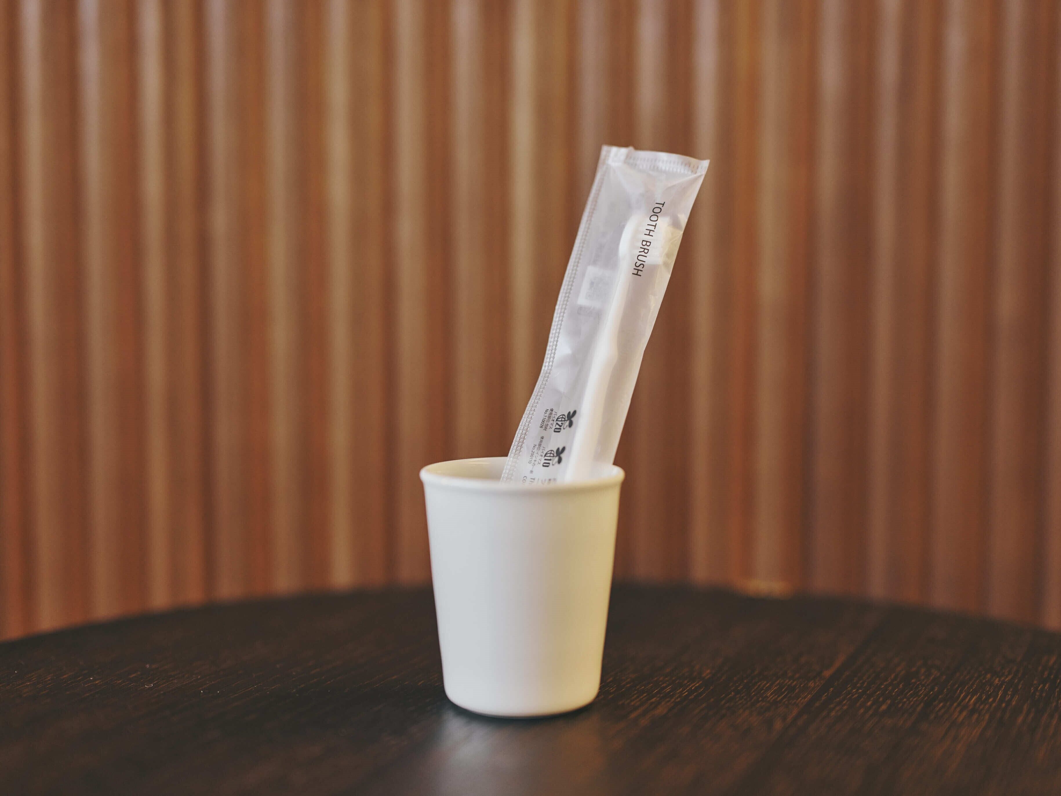 A white cup with a toothbrush and toothpaste tube on a wooden table.