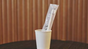 A white cup with a toothbrush and toothpaste tube on a wooden table.