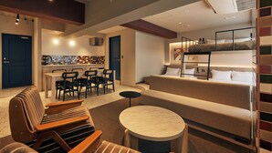 Una habitación de hotel moderna con sofá, una mesa redonda, literas y una kitchenette.