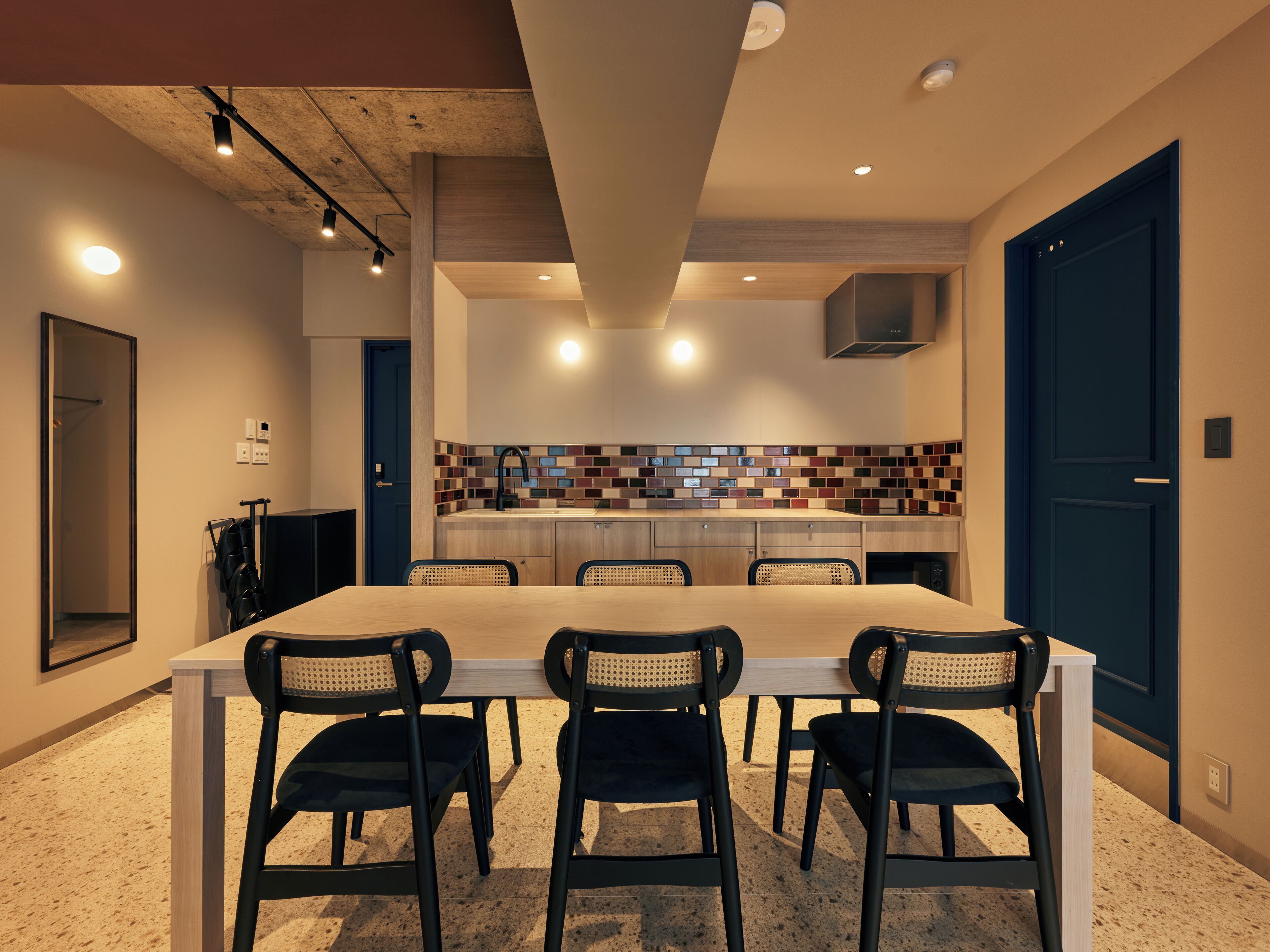 A modern kitchen with a tiled backsplash, a dining table with four chairs, and a blue door.
