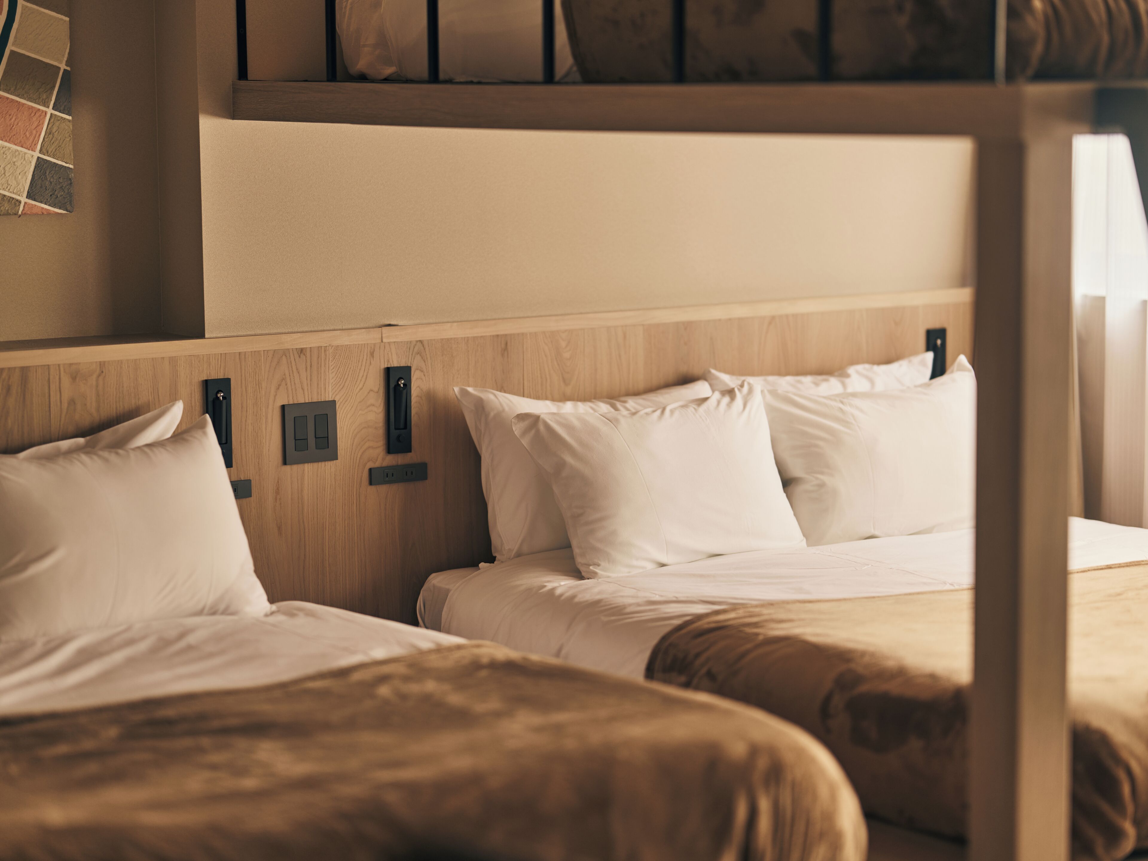 A hotel room with two beds, wooden headboards, and a small shelf with a clock and a book.