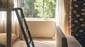 Una habitación con literas, una ventana con cortinas, una pared de ladrillo y una pequeña mesa redonda.