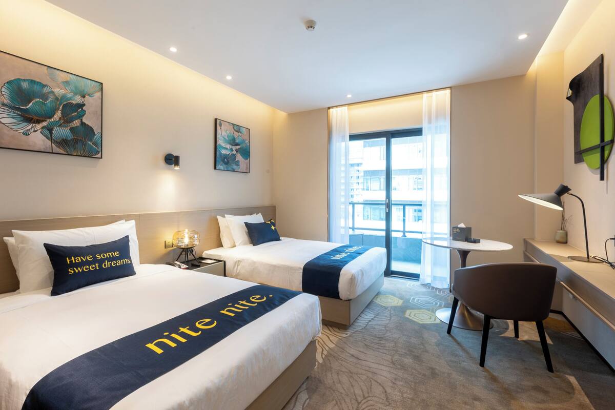 Une chambre d’hôtel avec deux lits, un bureau, une chaise et une vue sur la ville.