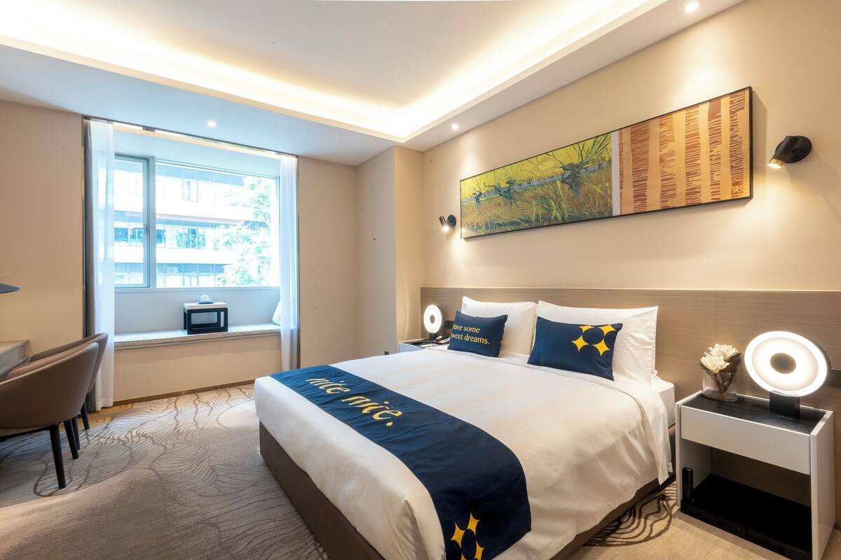 Une chambre d’hôtel avec un grand lit, des tables de chevet, un bureau et une fenêtre donnant sur un beau paysage.