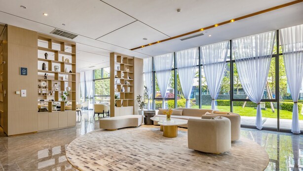 A modern hotel lobby with a reception desk, seating area, and large windows with sheer curtains. - Mulianzhuang Hotel FrontierMedicalCenter (Chengdu)