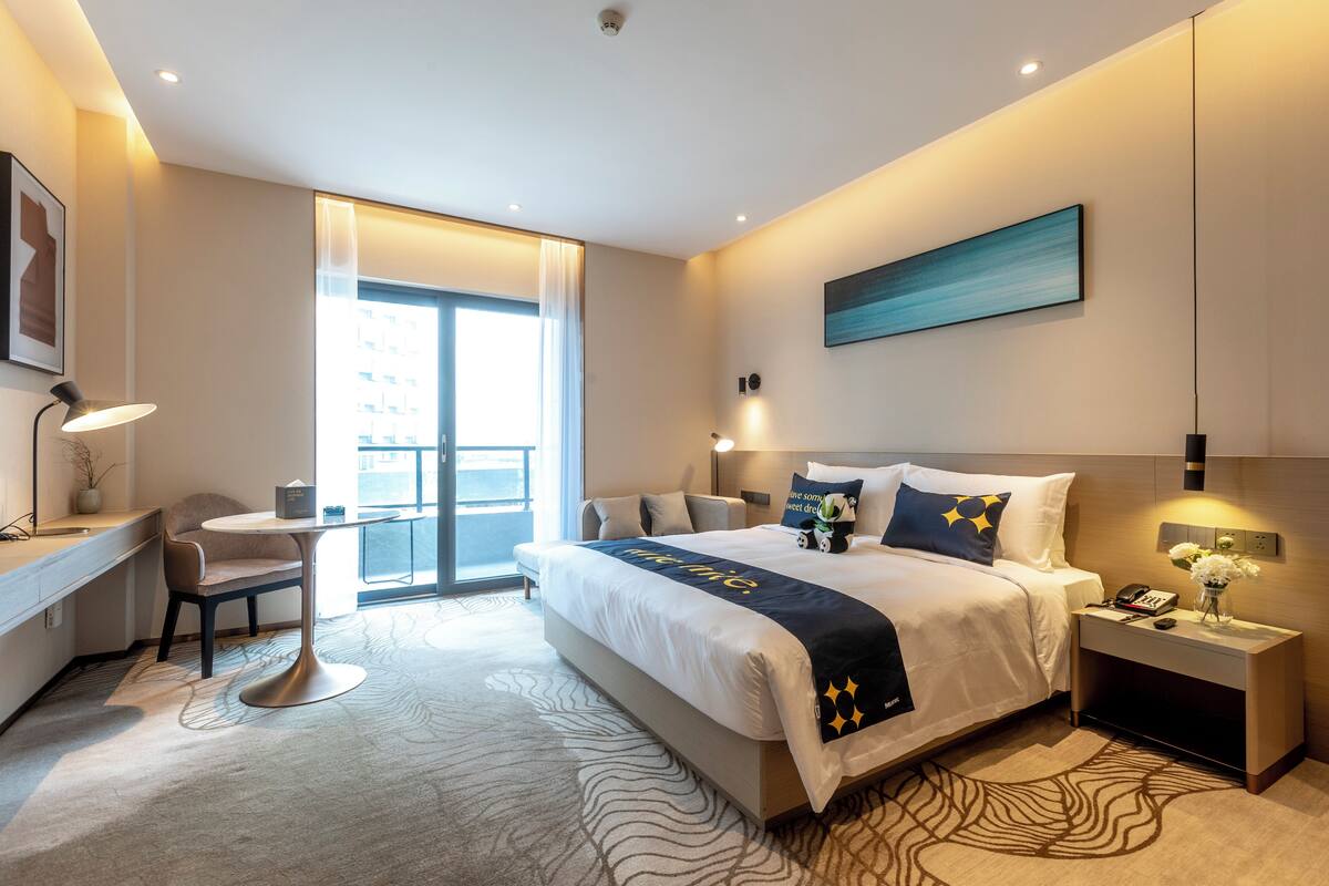 Une chambre d’hôtel moderne, dotée d’un grand lit, d’un bureau, d’une chaise et offrant une vue sur la ville.
