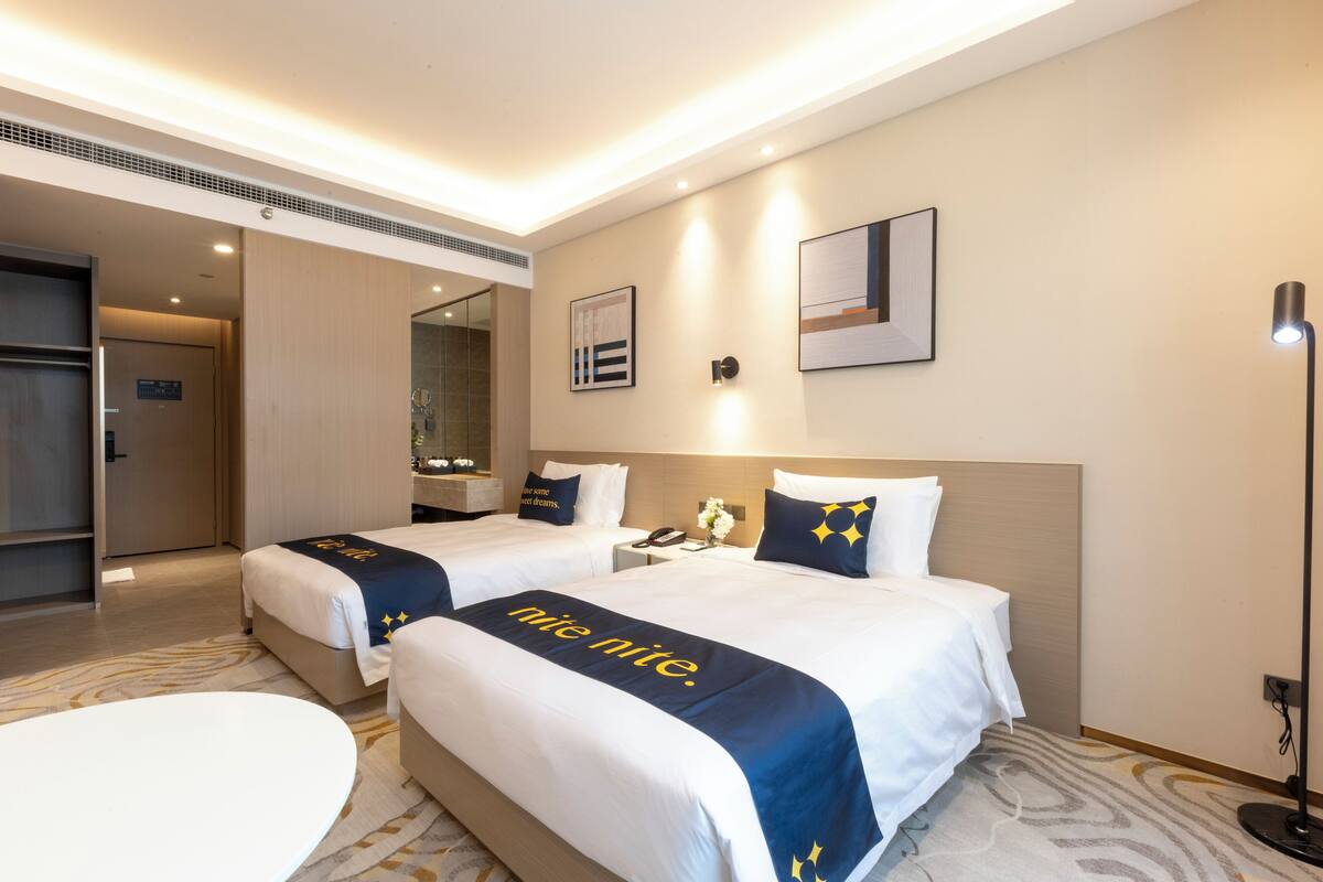 Une chambre d’hôtel avec deux lits, un bureau, une chaise et un grand miroir.