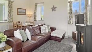 En hyggelig stue med en brun lædersofa, et spisebord med stole, en pejs og udsigt ud af vinduet.