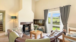 Un salon chaleureux avec une cheminée, un canapé, une table basse et une vue sur l’extérieur.