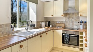 Une cuisine moderne dotée d’un four encastré, d’un évier et d’une fenêtre donnant sur les arbres.