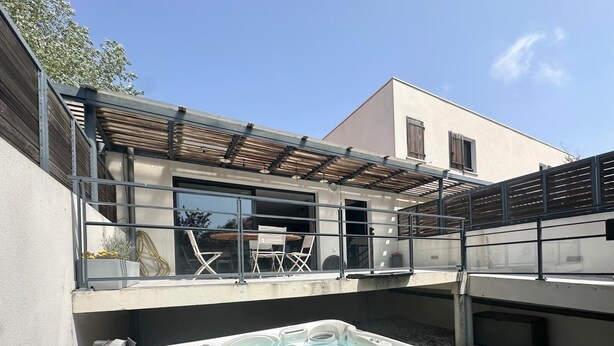 A modern outdoor hot tub area with a pergola, seating, and a view of the house. - Cocooning villa with jacuzzi (Le Grau-du-Roi)