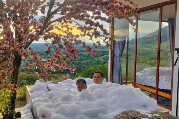 A room with a large window, a bed, and a tree with pink flowers. - Sirine Onsen (Khao Kho)