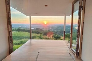A room with a large glass door leading to a balcony with a scenic view of a sunset over a valley. - Sirine Onsen (Khao Kho)
