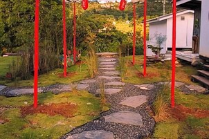 Un sendero en un jardín con postes rojos, un edificio blanco y una zona con baldosas de piedra.