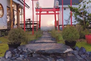 A pathway leading to a building with a red entrance archway, surrounded by potted plants and a stone pathway. - Sirine Onsen (Khao Kho)