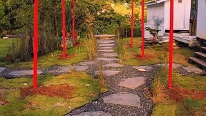 Un chemin de jardin bordé de poteaux rouges, un bâtiment blanc et un sentier en pierre.